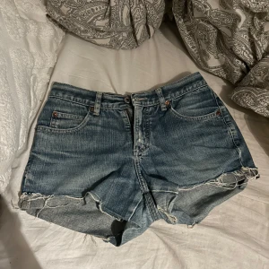 Blå jeansshorts från Guess - Säljer ett par snygga blå jeansshorts från Guess i bra skick. De har en fransig kant och klassisk femficksdesign. Perfekta för sommardagar eller festivaler! Storlek 27
