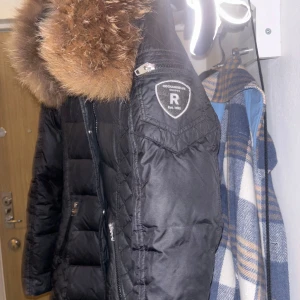 Svart dunjacka med pälsdetaljer - Säljer en snygg svart dunjacka från Rockandblue med en fluffig pälsdetalj på kragen. Jackan har en quiltad design och dragkedja framtill. Perfekt för kalla vinterdagar! 🖤