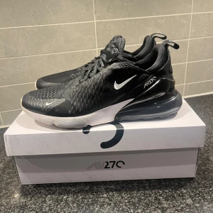 Svarta Nike Air Max 270 - Säljer ett par svarta Nike Air Max 270 i bra skick. De har en snygg design med en stor synlig Air-enhet i hälen för extra komfort. Ovandelen är i syntetmaterial med snörning för en säker passform. Perfekta för både vardag och träning! Vid fler frågor hör gärna av dig och vid snabb affär kan priset diskuteras. 