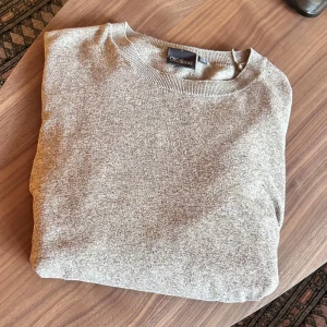 Beige tröja från Oscar Jacobson - Säljer en stilren beige tröja från Oscar Jacobson i storlek L, men en passar nästan som en M. Tröjan har en klassisk design med ribbade kanter. Perfekt för både vardag och lite finare tillfällen. Passar bra till höst och vår!