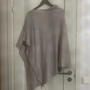 Beige glittrig poncho från Stockh LM - Säljer en superfin beige poncho från Stockh LM. Den har en glittrig yta som ger en extra touch av glamour. Perfekt för både vardag och fest! Ponchon är i mycket bra skick och passar perfekt till höst och vår.