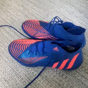 Säljer ett par Adidas Predator fotbollsskor i en cool blå och orange färgkombination. Skorna har en snygg design med snörning och är perfekta för fotbollsträning eller match. De är i bra skick och redo för nya äventyr på planen! Nypris 2300kr