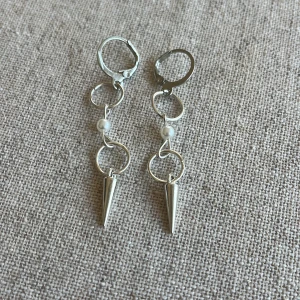 Silvriga örhängen med pärlor och konformade hängen - Snygga och unika silvriga örhängen med en kedja av ringar och små vita pärlor. De har coola konformade hängen längst ner som ger en edgy look. Perfekta för att piffa upp vilken outfit som helst!