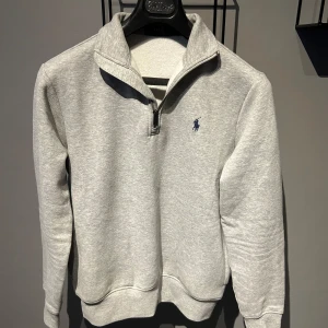 Grå tröja från Polo Ralph Lauren - Säljer en stilren och bekväm grå tröja från Polo Ralph Lauren. Den har en halv dragkedja framtill och en liten broderad logga på bröstet. Perfekt för både vardag och lite finare tillfällen. Tröjan är i nyskick och passar perfekt till höst och vår.