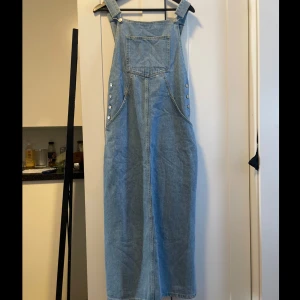 Jeansklänning med hängslen - Säljer en supercool jeansklänning med hängslen. Den är i en ljusblå denimfärg och har knappar på sidorna för en snygg detalj. Perfekt för en avslappnad sommarlook! 🦋Köpt för 499kr säljer för endast 180kr
