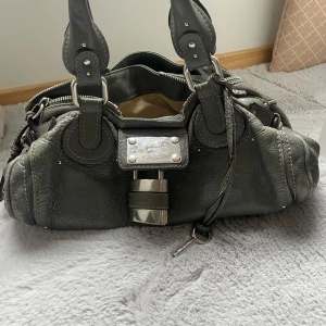 Chloe paddington väska - Jättefin väska från chloe paddington. Färg: mörkgrön/grå se bilder! Fint skick, finns några skavanker såsom att färgen är lite skavd på sidorna men inget som syns när man använder den. Även lite ”smutsig” inuti men inte särkilt mkt. Nypris på väskan ligger på ca 15000 kr. Äkthetbevis finns.