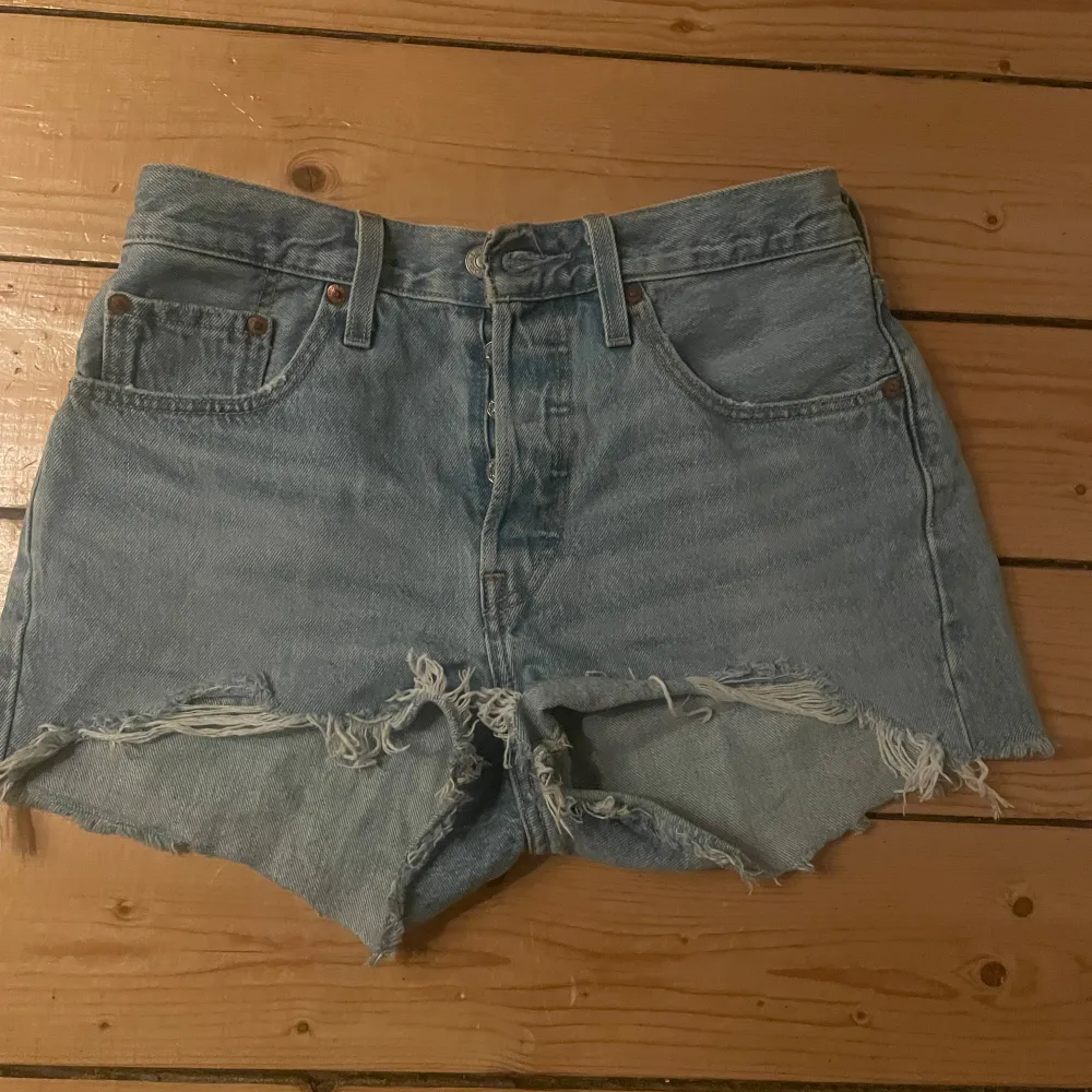 Säljer ett par coola jeansshorts från Levi's i ljusblå denim. De har en klassisk femficksdesign och är avklippta med råa kanter för en avslappnad look. Perfekta för sommardagar eller festivaler!. Shorts.