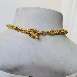 Guldigt halsband med tvinnad design - Säljer ett snyggt guldigt halsband med en cool tvinnad design. Perfekt för att ge lite extra bling till din outfit! Halsbandet har en chunky kedja som verkligen står ut och ger en lyxig känsla. Passar både till vardags och fest.