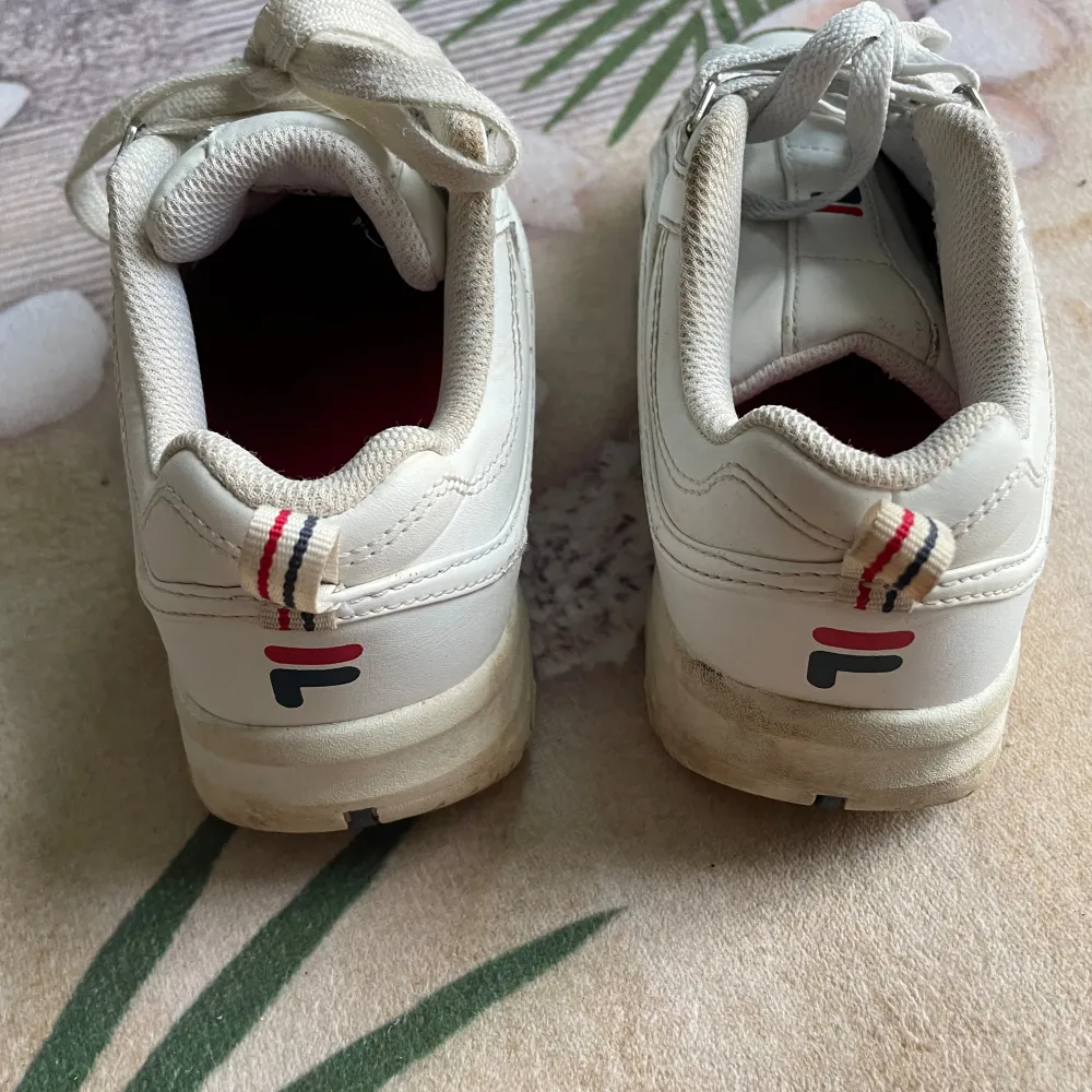 Säljer ett par vita Fila sneakers i bra skick. De har en klassisk design med snörning och Fila-loggan på sidan. Skorna är bekväma och perfekta för vardagsbruk. De har en stabil sula och är gjorda i syntetmaterial.. Skor.