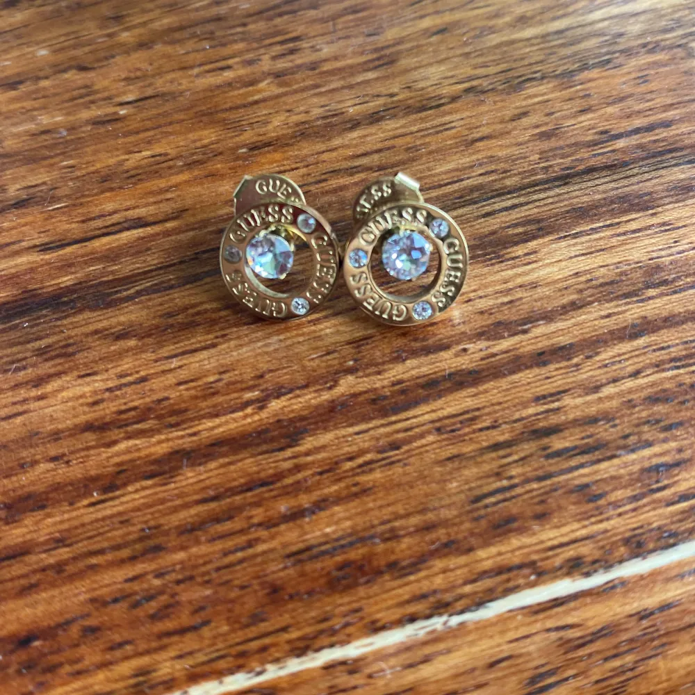 Säljer ett par snygga guldörhängen från Guess. De har en rund design med glittrande kristaller i mitten och runt om. Perfekta för att ge en touch av glamour till vilken outfit som helst. Kommer med originalpåse och certifikat.. Asusteet.