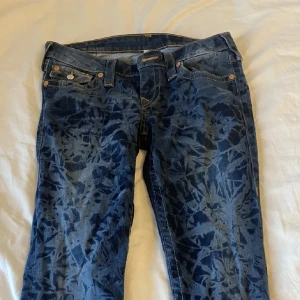 Mönstrade jeans från True Religion - Säljer ett par snygga blå jeans från True Religion. De har en låg midja och en straight passform. Jeansen är i bra skick. Det utsydda vid benen märks klart inte när man har på dem.