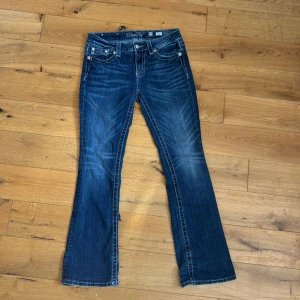Blå bootcut jeans från Miss Me - Säljer ett par lågmidjade snygga blå bootcut jeans från Miss Me. De har en cool design med detaljerade knappar och broderad logga på bakfickan. Perfekta för en avslappnad men stilren look! STORLEK: S-M funkar som båda!!