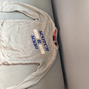 Grå tröja från Scotch & Soda - Säljer en snygg grå tröja från Scotch & Soda. Den har ett coolt tryck i blått och vitt på framsidan. Tröjan är långärmad och perfekt för en avslappnad stil. Passar bra till både jeans och chinos! Ny pris 500