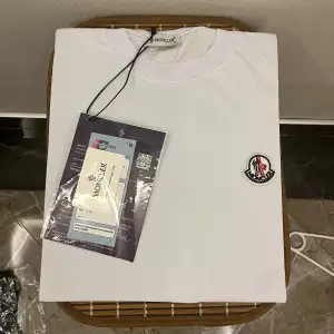 Säljer en snygg vit t-shirt från Moncler. Den är kortärmad och har en broderad Moncler-logga på bröstet. Perfekt för en stilren och avslappnad look. T-shirten är i bomull och känns riktigt skön mot huden.