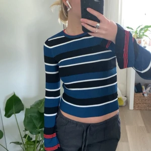 Randig stickad tröja från Zara - Säljer en superfin randig tröja från Zara i blått, svart och vitt med coola röda detaljer vid halsen och ärmsluten. Den är stickad och har en tight passform som sitter snyggt på kroppen. Perfekt för både vardag och fest!