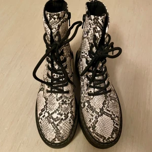 H&M Divided Kängor, Ormskinnsmönster, Storlek 37 - Perfekta till hösten! Stl 37 (innermått 23,5 cm). Snygga kängor från H&M Divided i vit/svart/grå. Kängorna har snörning och dragkedja på sidan, de har en platåsula och är ofodrade. Provade ute en gång. Nypris: 399 sek, Pris nu: 70 sek 