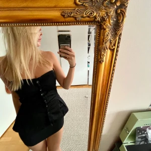 Svart axelbandslös klänning - Säljer en snygg svart axelbandslös topp/korsett med knappar framtill. Den har en tight passform och är perfekt för fest!  Köpt secondhand och om du har några fler frågor är det bara att kontakta mig 🌸