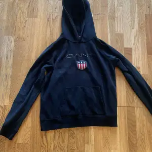 Säljer en snygg svart hoodie från GANT. Den har en cool logga med stjärnor och ränder på bröstet och en stor ficka framtill. Perfekt för höst och vinter, och den är superbekväm att ha på sig. Passar perfekt för en avslappnad stil!