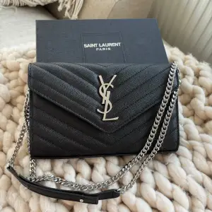 Säljer en superfin svart axelväska från Saint Laurent. Den är quiltad med ett snyggt mönster och har en silverkedja som axelrem. Väskan är i skinn och har en elegant YSL-logga på framsidan. Helt ny och oanvänd. Dm för mer info.