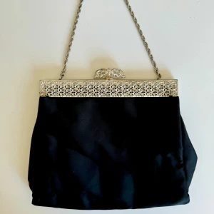 Elegant svart kuvertväska med silverdetaljer - Nyskick och BILLIG! Söt svart kuvertväska, festväska med silverkedja och vackra detaljer. Vit insida och rymlig nog för tex en IPhone 14pro max, nycklar + läppstift . Typ saltintag.Perfekt för fest! Mått, se bild. Hämtas på Hägerstensåsen eller ök 🖤✨