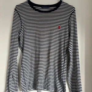 Randig långärmad tröja från Ralph Lauren - Säljer en snygg och klassisk randig tröja från Ralph Lauren. Den är mörkblå och vit med långa ärmar och har det ikoniska röda logotypbroderiet på bröstet. Perfekt för både vardag och lite mer uppklädda tillfällen. 