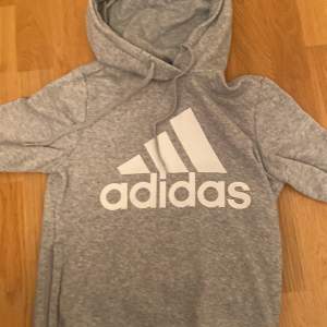 Säljer en superbekväm grå hoodie från Adidas i storlek XS. Den har en klassisk design med Adidas-loggan tryckt i vitt på framsidan. Perfekt för både träning och mysiga dagar hemma. Huvan är justerbar med snören och materialet är mjukt och skönt.