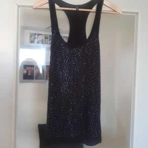 Svart glittrig linne - Snygg svart linne med glittriga detaljer, perfekt för festliga tillfällen. Den är ärmlös och har en tight passform som framhäver figuren. Materialet känns mjukt och bekvämt mot huden.