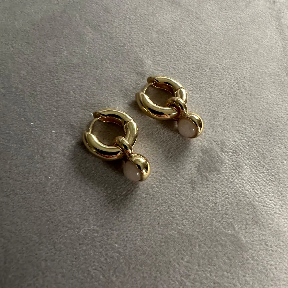 Guldpläterade, chunky ringar Hänge med äkta rosenkvarts Mått 22 mm i längd Trendiga med en touch av naturlig elegans Tillverkat av 95% återvunnet material. helt oanvända!!! nypris 449kr. Accessoarer.