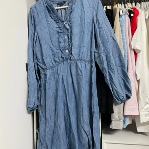 Blå klänning från Esmara - Säljer en superfin blå klänning från Esmara. Den har långa ärmar och en söt volangdetalj längs knäppningen framtill. Perfekt för en avslappnad dag eller en somrig utflykt. Klänningen är i ett mjukt och bekvämt material som känns skönt mot huden.