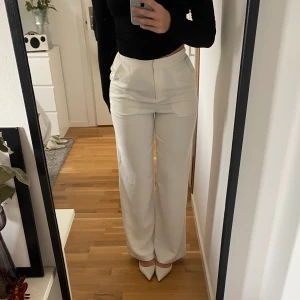 Vita högmidjade byxor - Säljer ett par stilrena vita byxor som är högmidjade och har en rak passform. De är superbekväma och ger en snygg siluett. Tyvärr har jag en knapp lossnat men inget som syns eller märks och kan lätt sys dit en ny, se sista bilden.