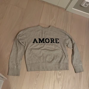 Grå tröja med texten AMORE - Långärmad beige tröja med texten amore. Har bara använt den några få gånger. 