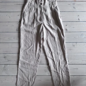 Beige linnebyxor med knappar - Säljer ett par snygga beige linnebyxor med hög midja och knappar framtill. Byxorna har en avslappnad passform och är perfekta för både vardag och fest. De är gjorda i ett lätt och luftigt material som passar bra till vår och sommar.