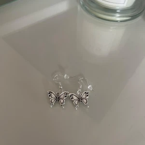 Silverfärgade fjärilsörhängen - Säljer ett par superfina silverfärgade örhängen formade som fjärilar. De har en detaljerad design med små utskärningar som ger dem en elegant look. Perfekta för att piffa upp vilken outfit som helst! 🦋