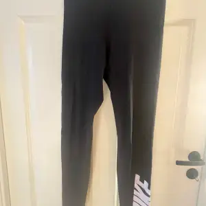 Säljer ett par svarta leggings från Nike i storlek S. De är perfekta för träning eller en avslappnad dag. Leggingsen har en hög midja och är gjorda i ett stretchigt material för bästa passform. Nike-loggan finns tryckt i vitt längs benet och i midjan.