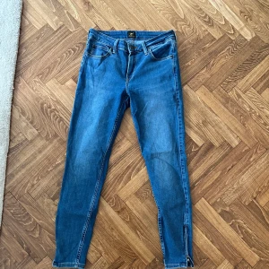 Lee jeans - Blåa Lee jeans med dragkedja vid sidan om smalbenet. Använda men i bra skicka  Storlek W27L31