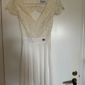 Vit spetsklänning från Chiara Forti - Säljer en superfin vit klänning från Chiara Forti i storlek XS. Den har en vacker spetsöverdel med korta ärmar och en v-ringning. Klänningen har en elegant öppen rygg som ger en extra touch av stil.