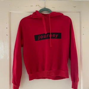 Röd hoodie från Gina Tricot - Säljer en snygg röd hoodie från Gina Tricot med texten 'journey' tryckt i svart på framsidan. Den har en skön luva med dragsko och ribbade muddar vid ärmslut och nederkant. Perfekt för en avslappnad stil!