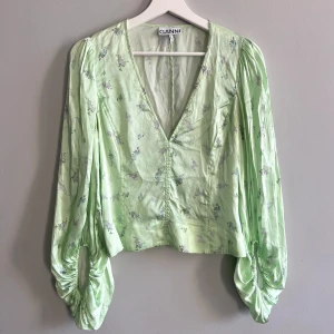Ganni Silkes topp - Grön silkes topp med vacker mönster från Ganni och knappt använd. V ringning och figursydd med vida armar Storlek: 38  Skriv om du har funderingar!