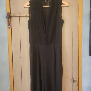 Säljer en elegant svart ärmlös byxdress från H&M. Byxdressen har en djup v-ringning och en dragkedja i ryggen. Perfekt för festliga tillfällen eller en utekväll. Materialet känns lätt och bekvämt att bära.