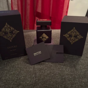 Initio Side Effect Eau de Parfum - Exklusiv parfym från Initio, Side Effect, i en elegant mörklila flaska med gyllene detaljer. Flaskan rymmer 90 ml och kommer i en lyxig förpackning med ett dekorativt mönster. Perfekt för den som söker en unik och sofistikerad doftupplevelse. Endast sprayad ca 5 gånger för att lukta på den.