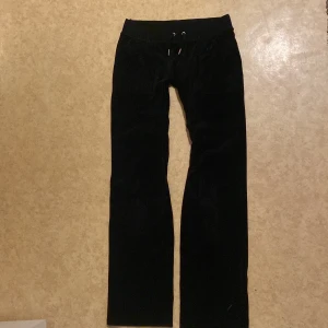 Svarta byxor från Juicy Couture - Snygga svarta byxor från Juicy Couture i mjukt material. Byxorna har en dragsko i midjan och broderad logga. Perfekta för en avslappnad stil. Det har sytts om lite vid innerbenssömnen.