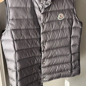 Grå dunväst från Moncler - Snygg grå dunväst från Moncler i storlek S med knappar och ett stilrent märke på bröstet. Dustbag ingår. Knappt använd, i toppskick! 