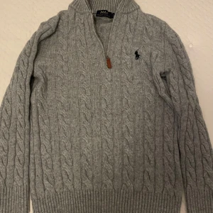 Grå kabelstickad tröja från Polo Ralph Lauren - Säljer en stilren grå kabelstickad tröja från Polo Ralph Lauren. Tröjan har en dragkedja vid halsen och det ikoniska logotypbroderiet på bröstet. Perfekt för kyliga dagar med sin mjuka och varma känsla. Lämna gärna prisförslag 😁