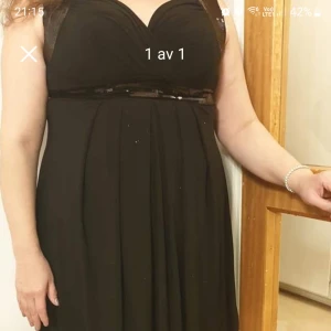 Svart klänning med v-ringning - Elegant svart klänning med v-ringad hals och ett smalt bälte i midjan. Klänningen har en klassisk och tidlös design som passar perfekt för festliga tillfällen.