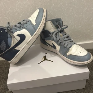 Nike Air Jordans i blått och vitt - Snygga Nike Air Jordans i en stilren kombination av blått och vitt. Skorna har klassisk snörning och är tillverkade i skinn. Perfekta för dig som vill ha en sportig och trendig look.