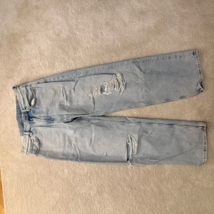 Baggy  jeans med slitningar - Snygga ljusblå jeans med slitningar på låren och knäna. Baggy jeans. Storlek 31/32. Byxan är i mycket bra skick och är knappt använd.