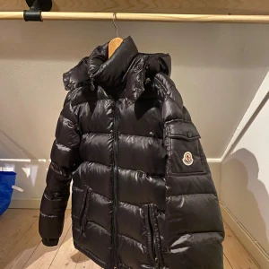 Moncler maya - Hejsan! Säljer min Moncler Maya av äldre modell då jag vuxit ur den. Snygg och passar till vintern men även hösten och våren. Säljer till ett billigt pris då den har två slitningar och har själv köpt den Vintage för några år sedan och har därför inget äktehetsbevis eller garanti. Mycket skön och varm och är i gott skick förutom två slitningar. En pricka som är lagad med svart gaffa tejp på framsidan. Men eftersom jackan är glansig så syns knappt detta. Även en av spännbanden på luvan är löst. 