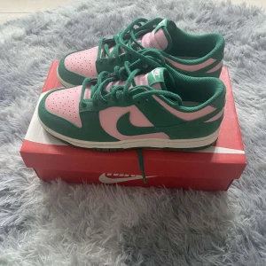 Nike Dunk Low Retro SE i rosa och grönt - Snygga Nike Dunk Low Retro SE sneakers i en fräsch kombination av rosa och grönt. Skorna har en klassisk design med snörning och en bekväm passform. Perfekta för att ge din stil en färgklick.