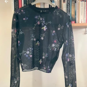 Svart blommig meshtröja - Snygg svart meshtröja med blommigt mönster i lila, rosa och grönt. Tröjan är knappt använd och har inga synliga defekter. 