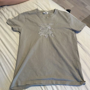 Grå t-shirt från Burberry - Snygg grå t-shirt från Burberry med ett stilrent broderat motiv på bröstet. Perfekt för en avslappnad fit